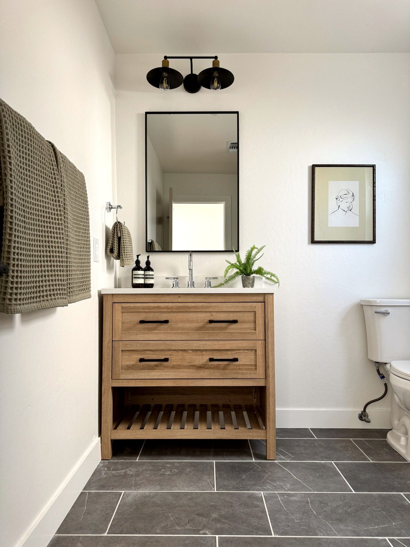 Martinez bathroom with wood vanity, dark floor tile, and black-framed mirror