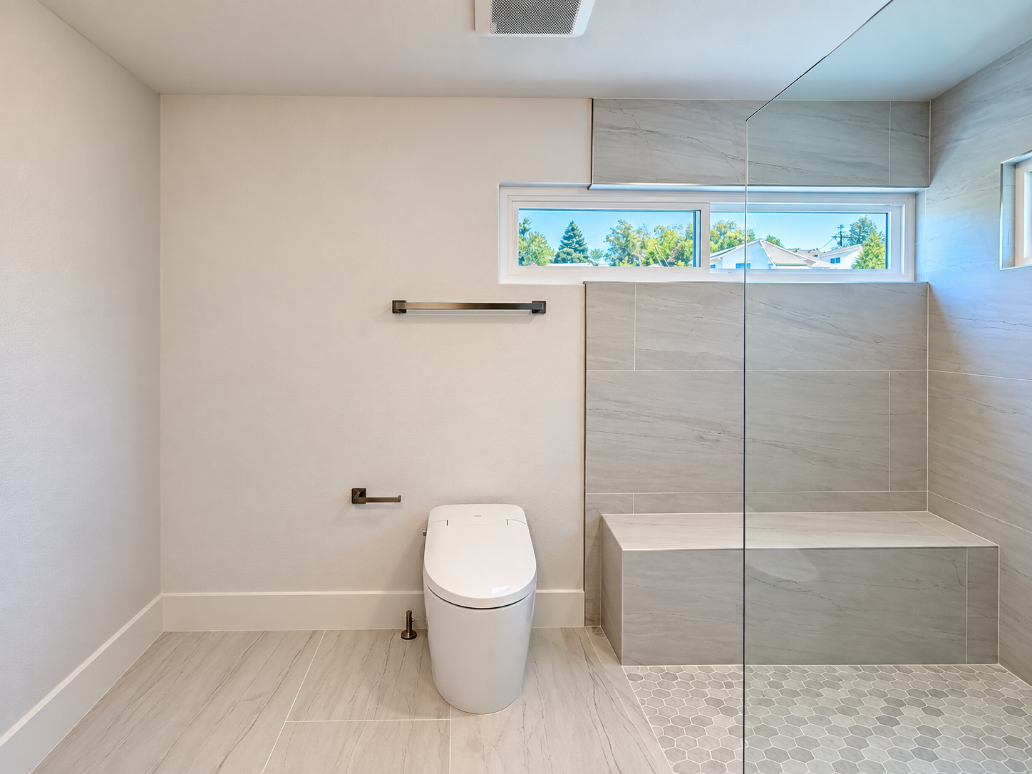 Primary bathroom view showing shower bench, window and toilet