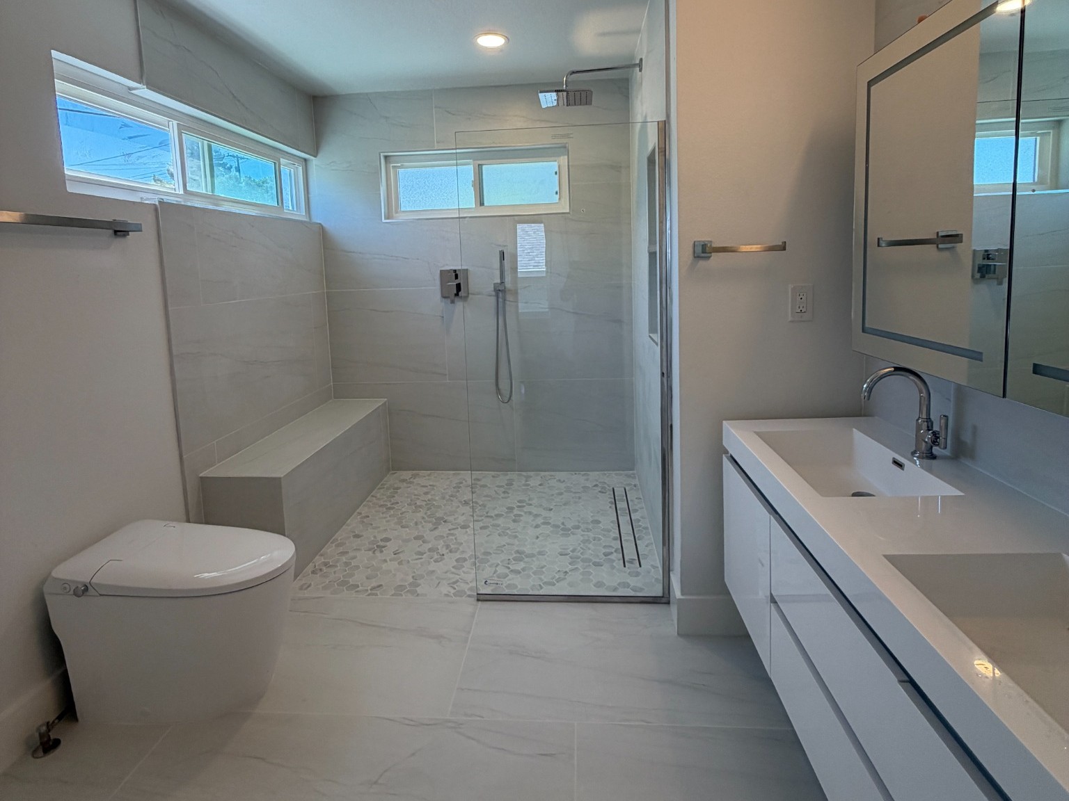 Primary bathroom overview with walk-in shower, shower bench, toilet and floating double vanity